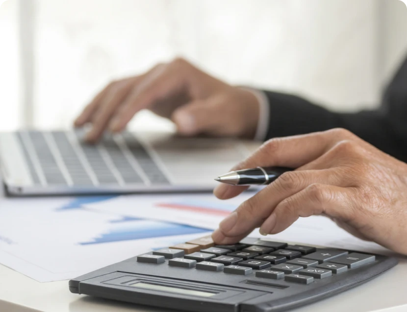Hands using calculator and laptop on desk.